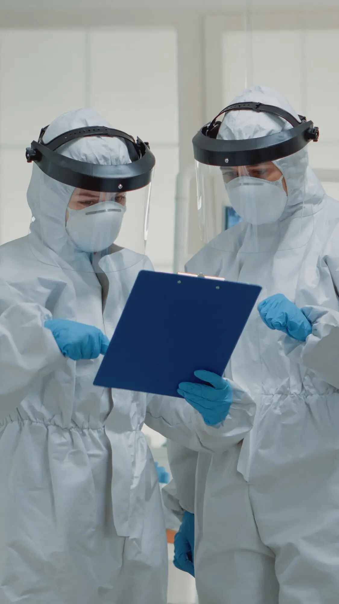 Врачи-стоматологи в защитных костюмах от COVID обсуждают уход за зубами пациента. Команда стоматологов в лицевых щитках обсуждает стоматологическую операцию в клинике.